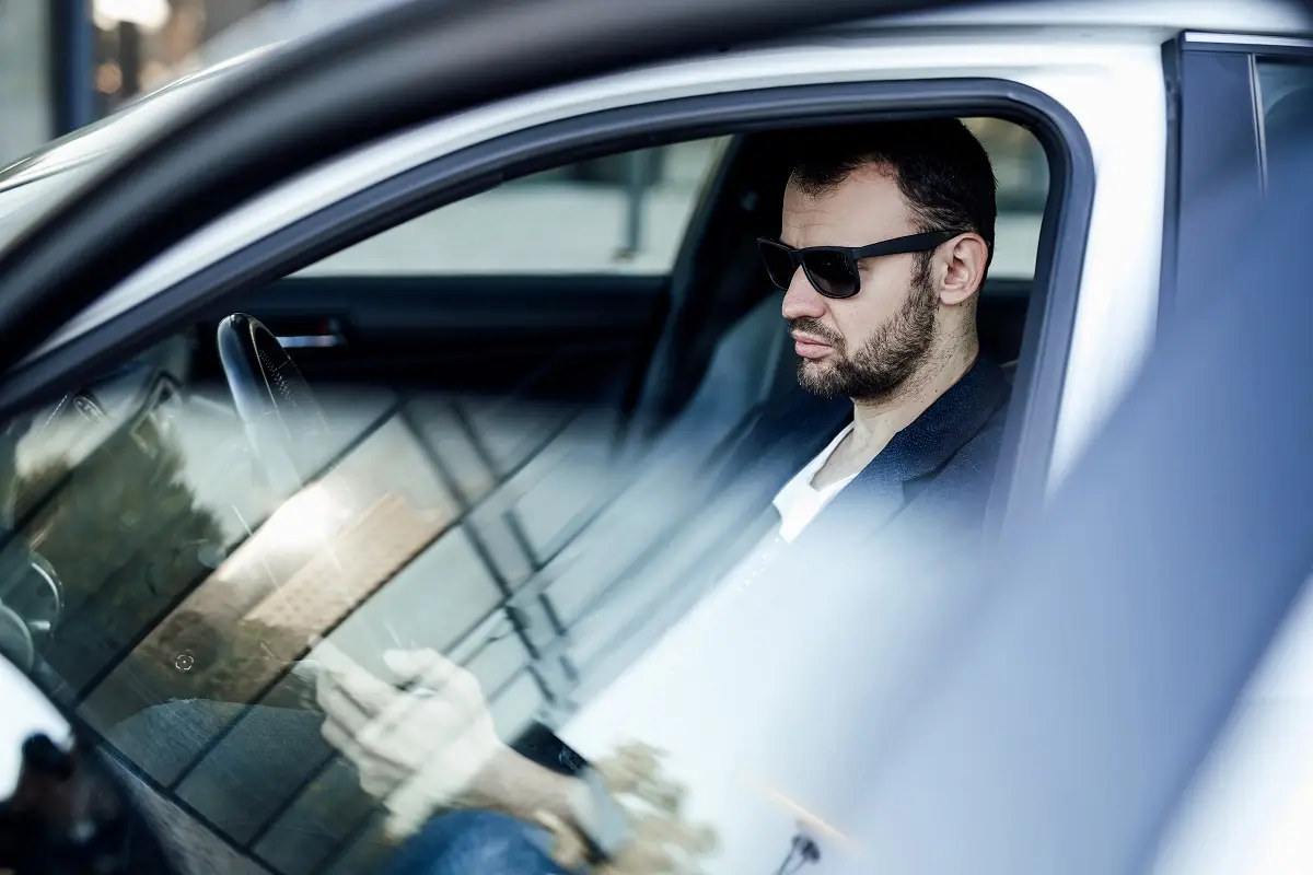Man in sunglasses sitting in a car, demonstrating the benefits of auto window tinting for UV protection and enhanced privacy.