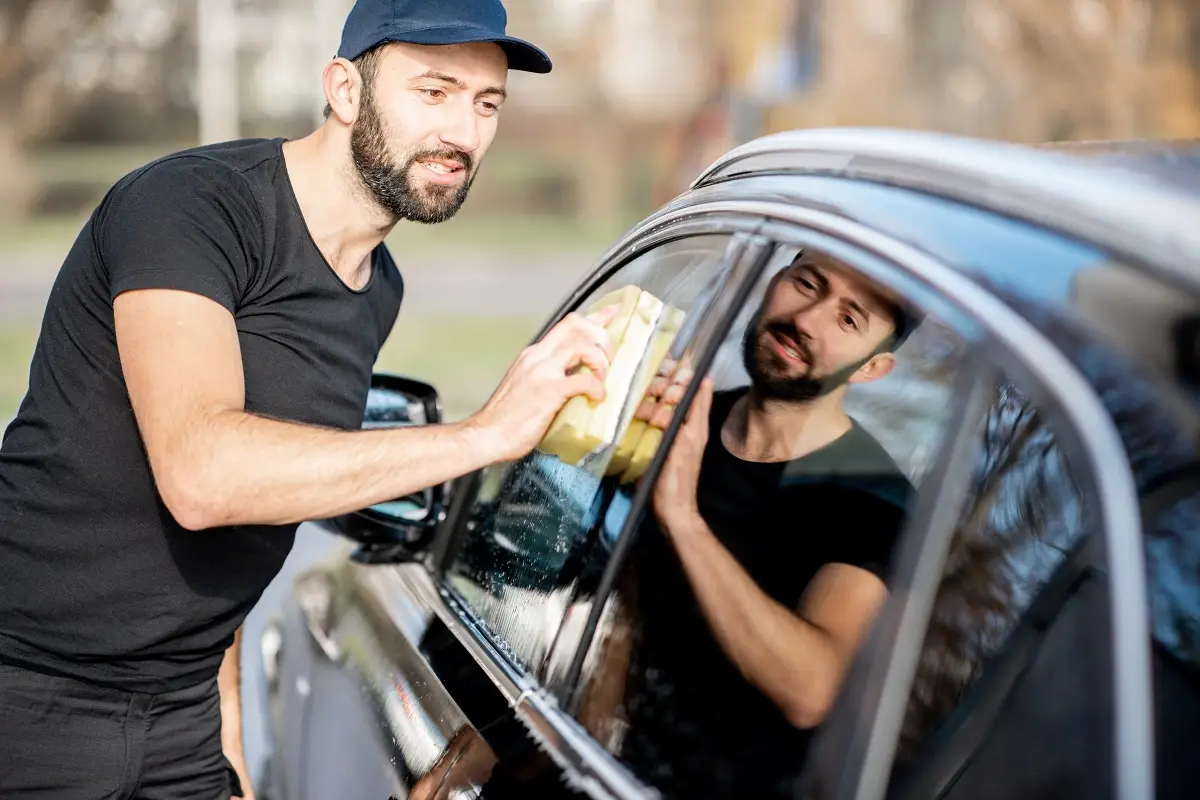 Man applying window tint to a car, enhancing vehicle privacy and security, demonstrating auto window tinting services.