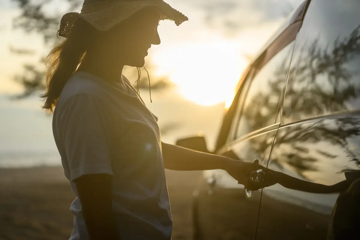Woman reaching for car door handle at sunset, highlighting vehicle aesthetics and privacy benefits of auto window tinting.