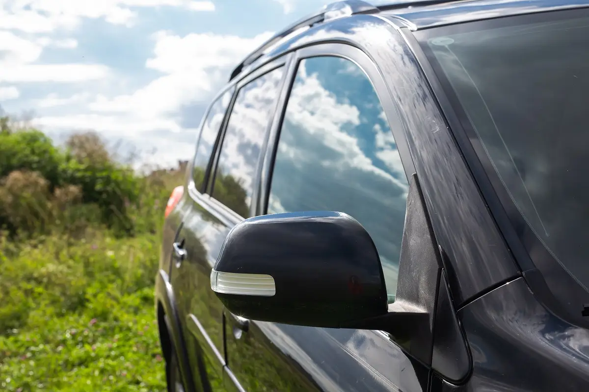 Black vehicle with tinted windows reflecting clouds and greenery, highlighting enhanced privacy and security features of auto window tinting.