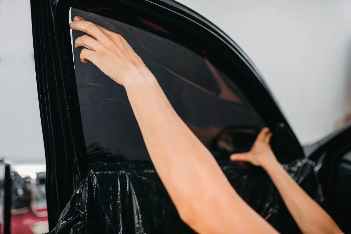 Person applying window tint film to a car door, demonstrating auto window tinting process for enhanced privacy and UV protection.